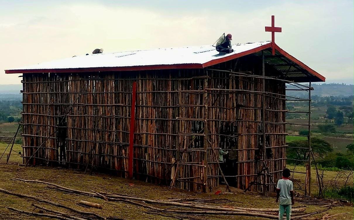 Completed church building with metal roof and cross, workers finishing the roofline